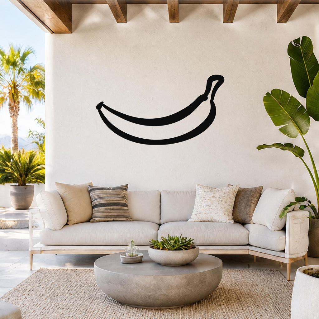 Black metal banana wall art silhouette mounted above a white sofa in a bright living room with wooden beams and tropical plants.