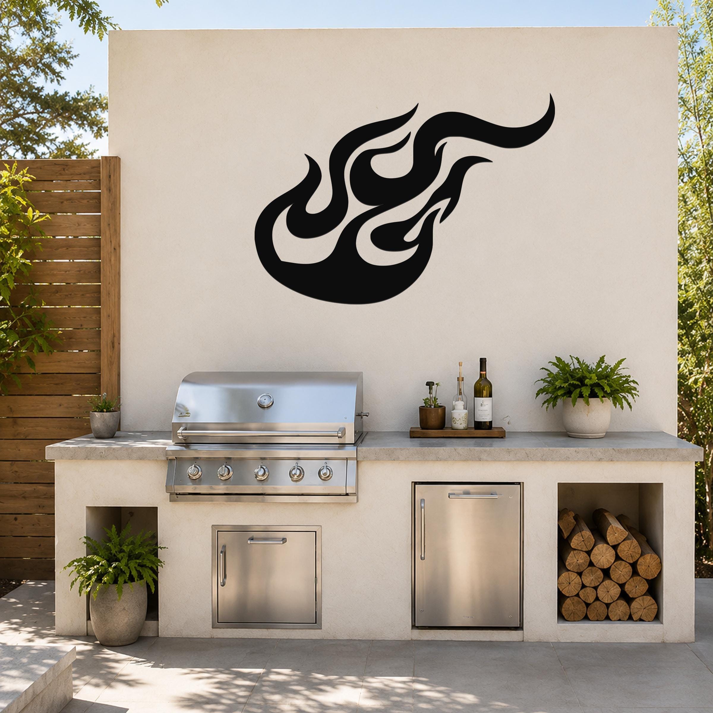 Black metal flame wall art with flowing silhouette design, mounted on an outdoor kitchen wall above a stainless steel grill and counter.
