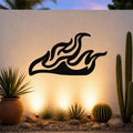 Black metal flame wall art with flowing silhouette cutouts, mounted on an outdoor wall above a desert garden with cacti and warm uplighting.