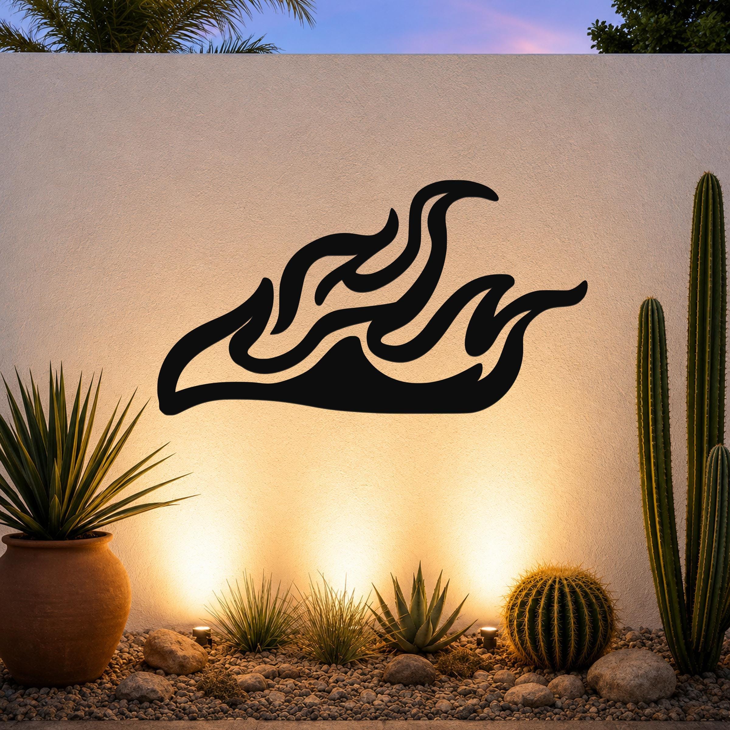 Black metal flame wall art with flowing silhouette cutouts, mounted on an outdoor wall above a desert garden with cacti and warm uplighting.
