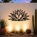 Black metal agave wall art with bold geometric cutouts, mounted on an outdoor wall above a desert garden with cacti and warm uplighting.