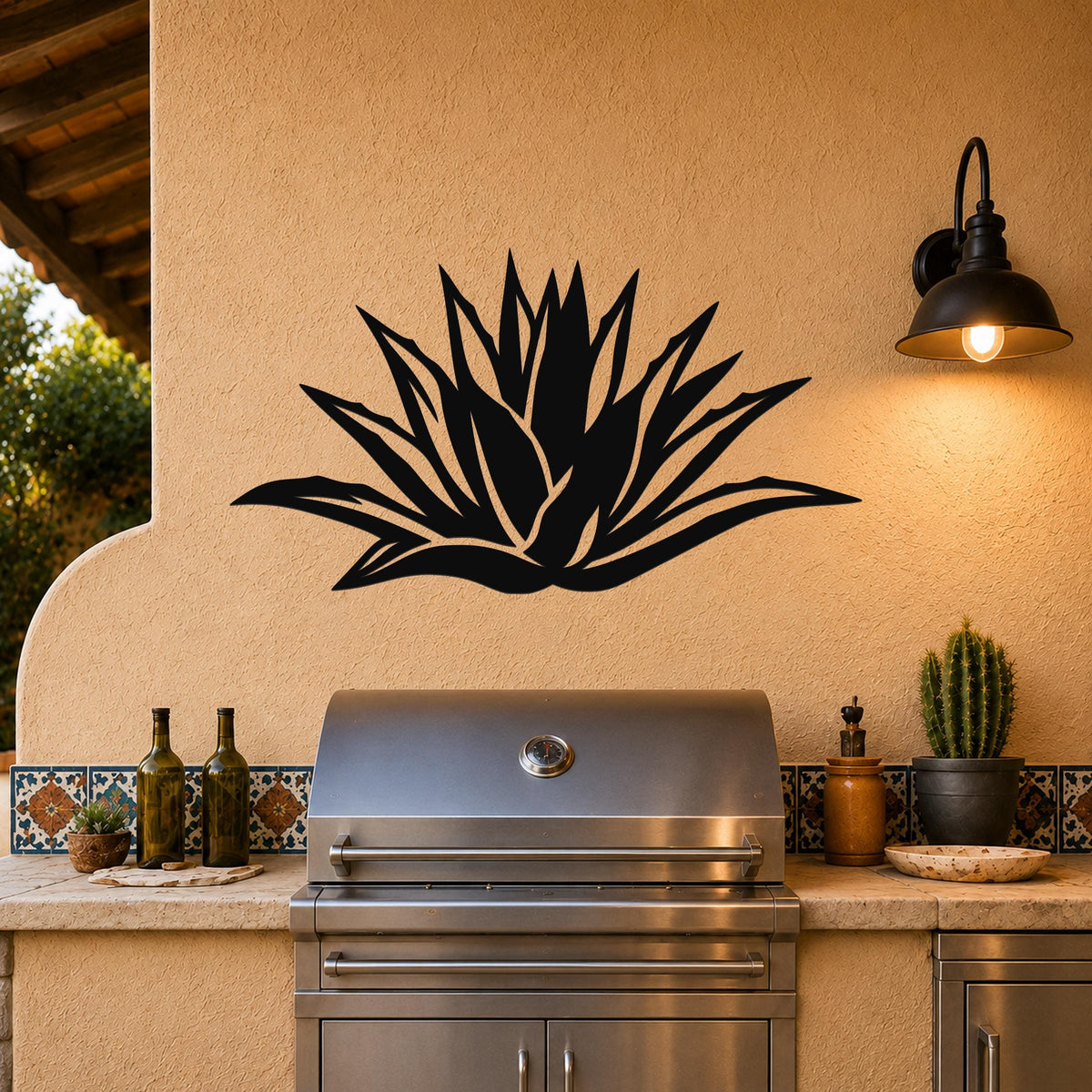 Black metal agave wall art with leaf cutouts, mounted on a stucco wall above a stainless steel grill on an outdoor patio.
