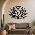 Black metal agave wall sculpture with layered leaf cutouts, mounted on a stucco wall above a wooden bench in a desert-style patio.
