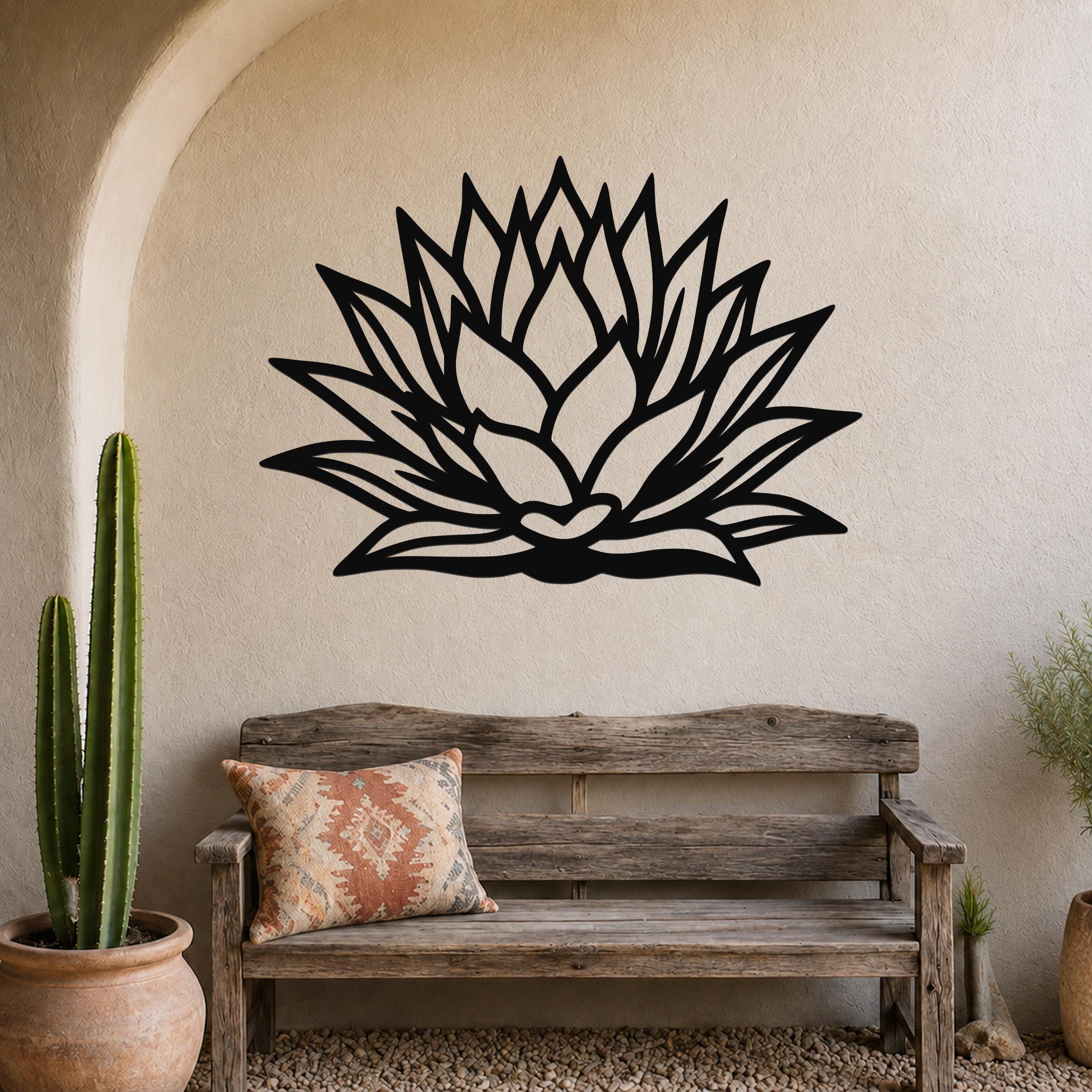 Black metal agave wall sculpture with layered leaf cutouts, mounted on a stucco wall above a wooden bench in a desert-style patio.