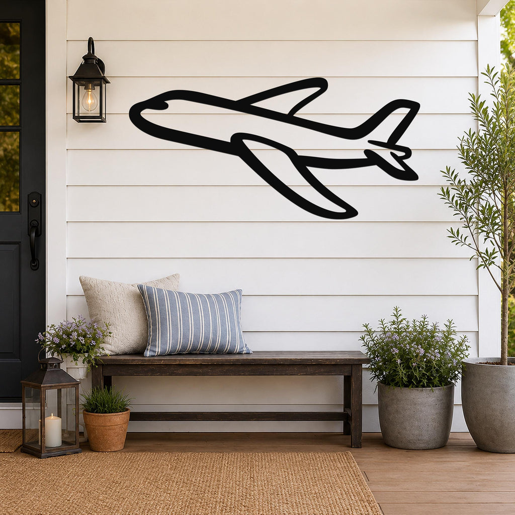 Black metal airplane wall art with bold silhouette design, mounted on a white shiplap wall above a wooden bench on a porch.