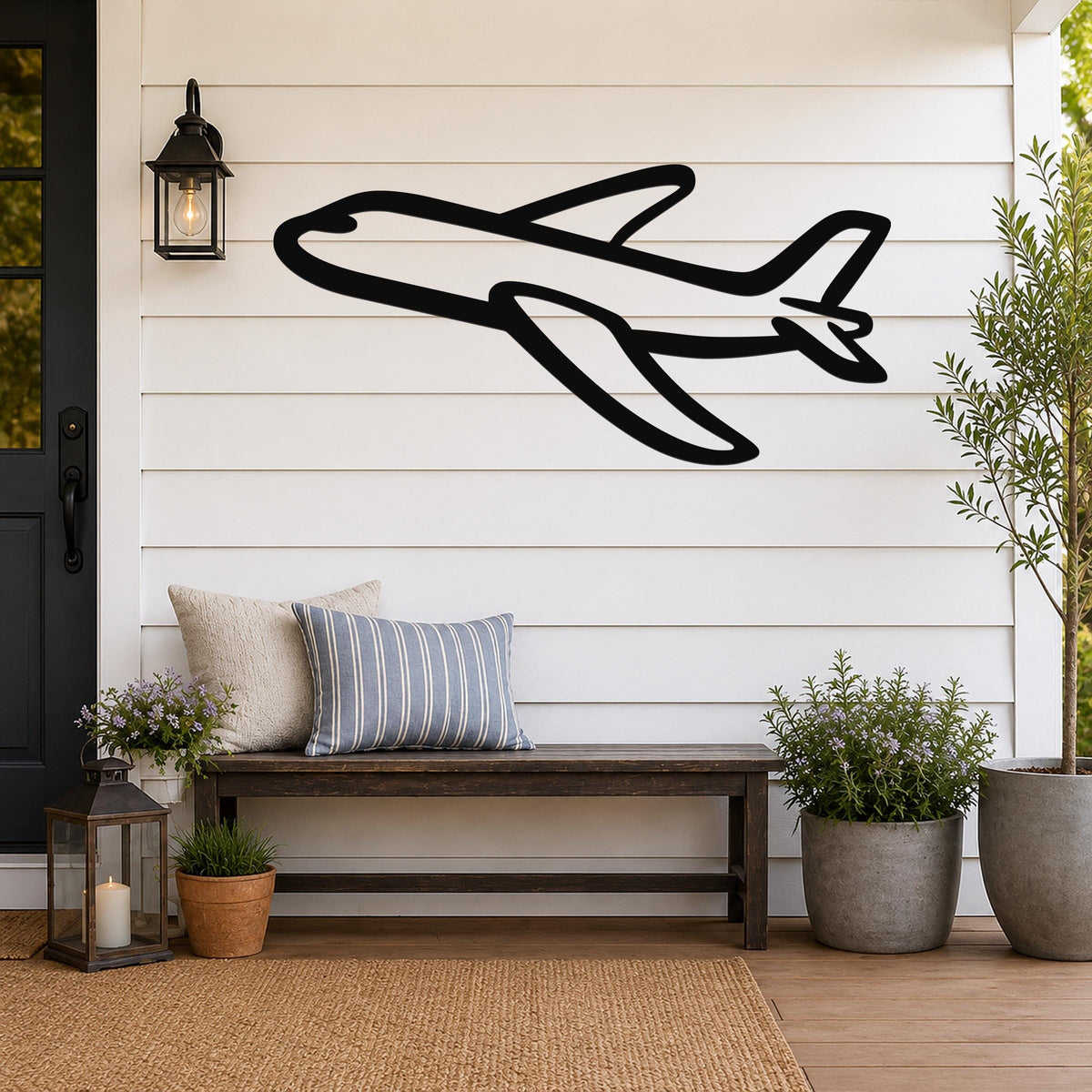Black metal airplane wall art with bold silhouette design, mounted on a white shiplap wall above a wooden bench on a porch.