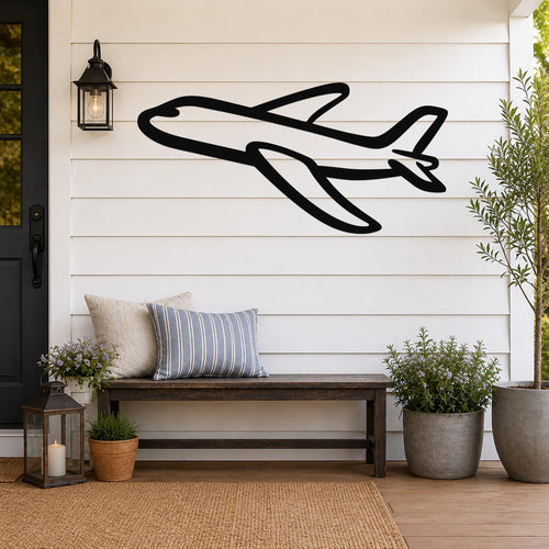 Black metal airplane wall art with bold silhouette design, mounted on a white shiplap wall above a wooden bench on a porch.