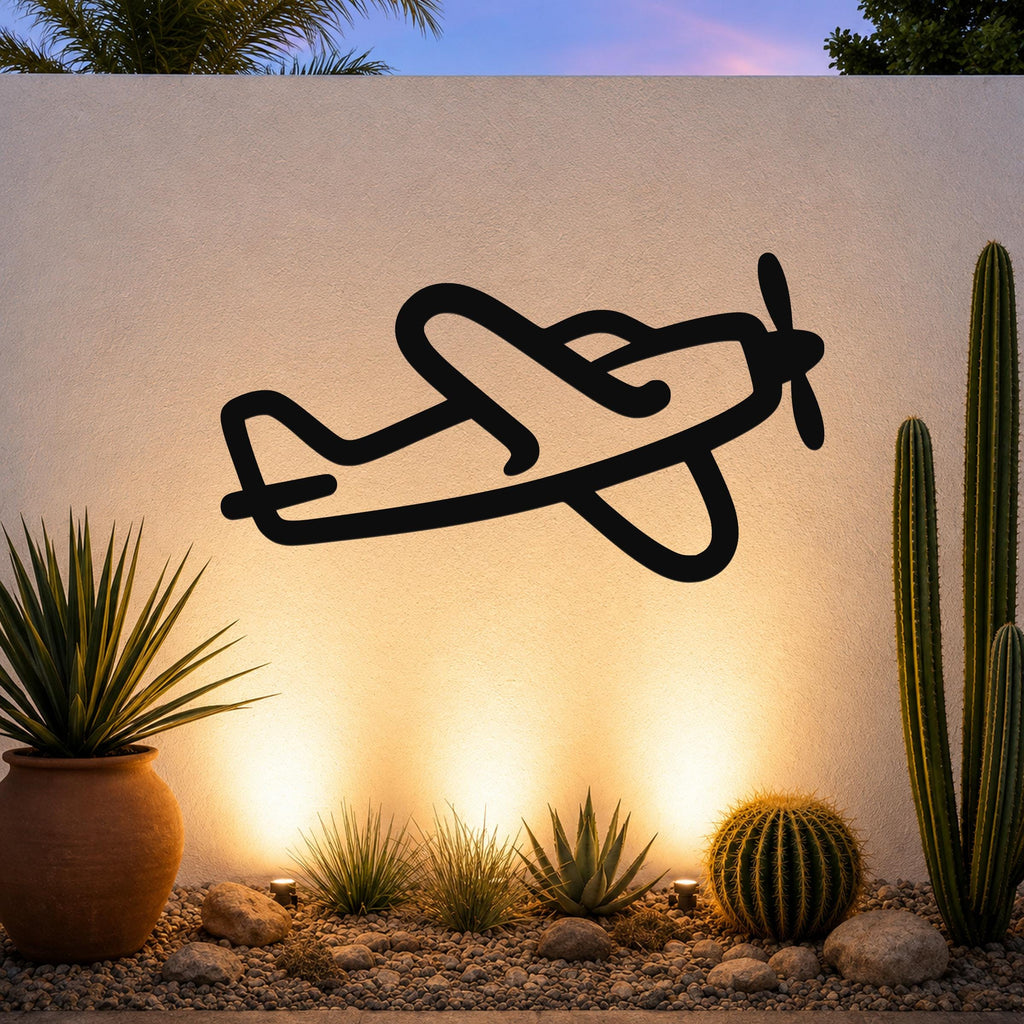 Black metal airplane wall art silhouette with propeller and wing cutouts, mounted on an outdoor wall above a desert garden with cacti and warm uplighting.