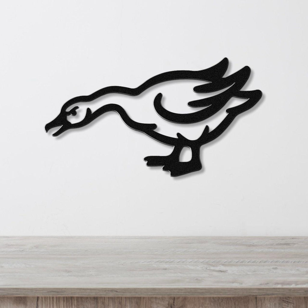 Black metal wall art cutout of a goose in motion, mounted on a white wall above a light wood surface.