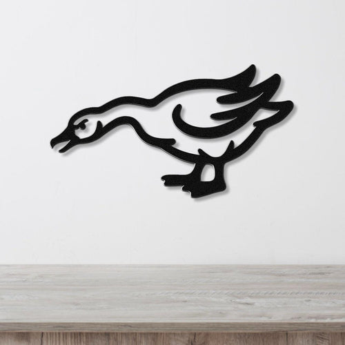 Black metal wall art cutout of a goose in motion, mounted on a white wall above a light wood surface.