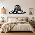 Black metal barrel cactus wall art with spines and rocks cutout, mounted above a bed in a neutral bedroom.