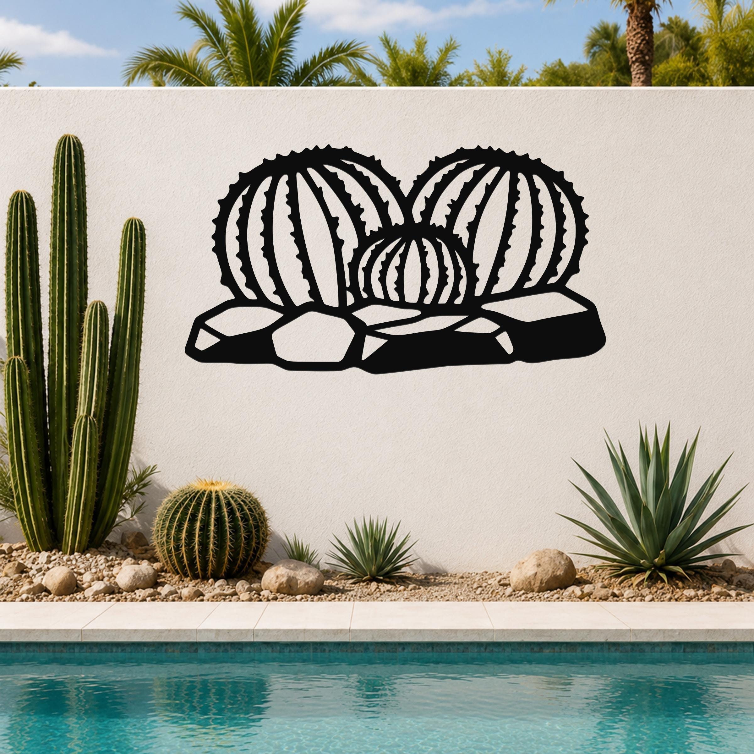 Black metal barrel cactus wall art with ribbed cutout design, mounted on a white outdoor wall above a poolside garden.