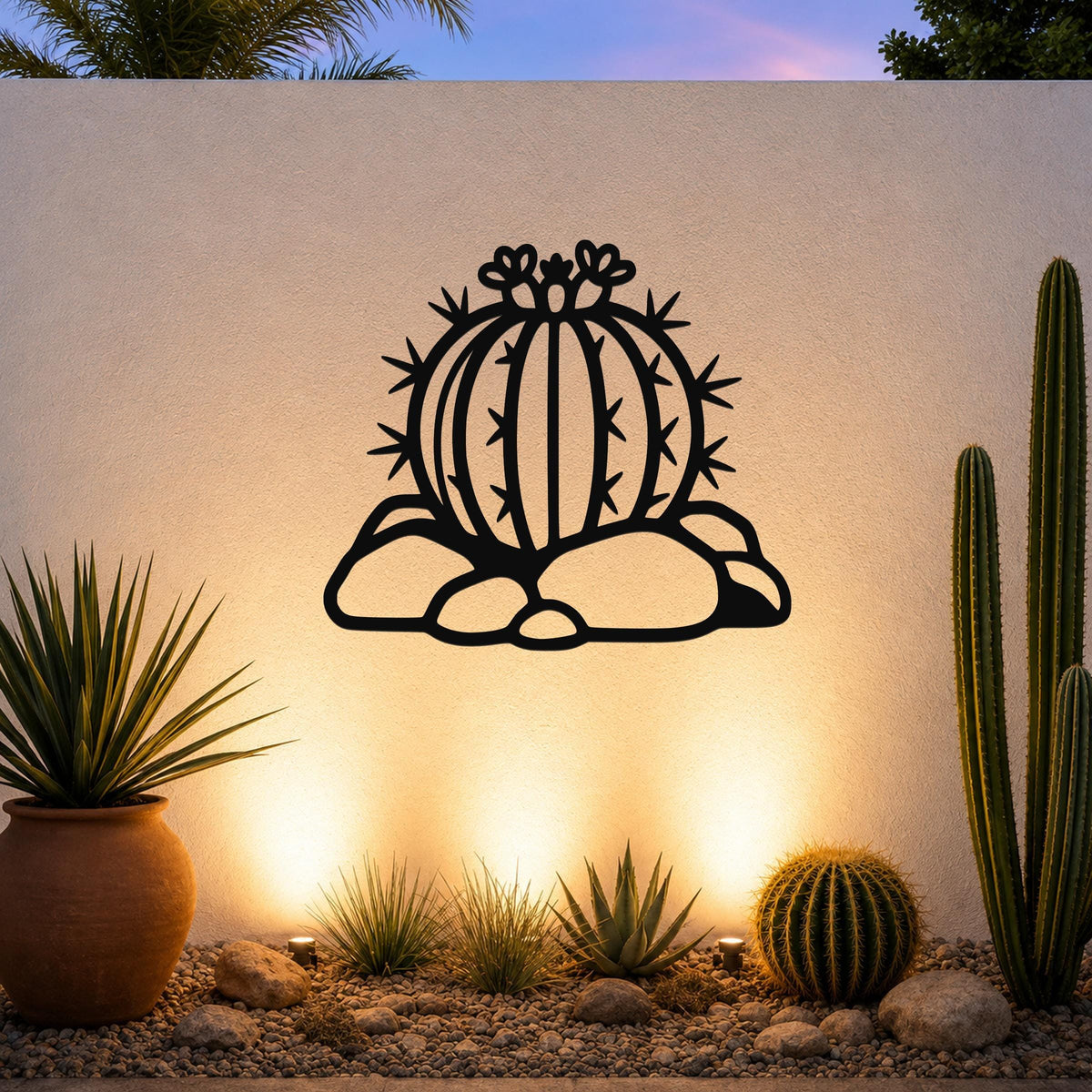 Black metal barrel cactus wall art with flower and spine cutouts, mounted on a white outdoor wall above a desert garden with potted plants and ground lights.