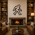 Black metal Bigfoot wall art silhouette with motion-line cutouts, mounted above a stone fireplace in a rustic living room.