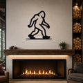 Black metal Bigfoot wall art silhouette mounted above a fireplace in a living room.