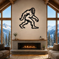 Black metal Bigfoot wall art silhouette with motion-line cutouts, mounted above a fireplace in a rustic living room with mountain views.