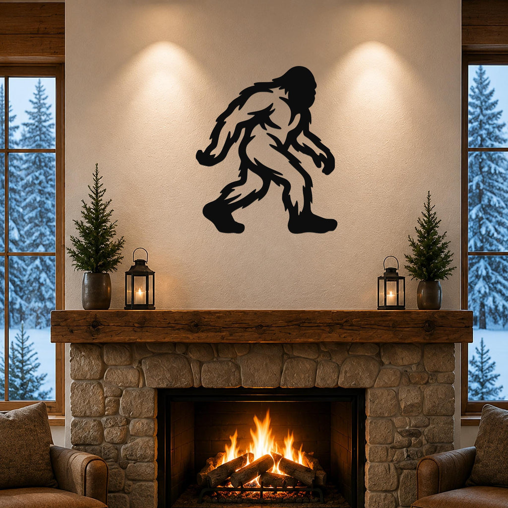 Black metal Bigfoot wall art silhouette mounted above a stone fireplace in a rustic living room with wooden beams and snow-covered trees visible through windows.