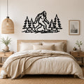 Black metal wall art silhouette of Bigfoot among pine trees, mounted above a bed in a bedroom.