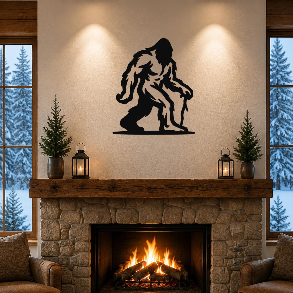 Black metal Bigfoot silhouette wall art mounted above a stone fireplace in a rustic living room with snow outside the windows.