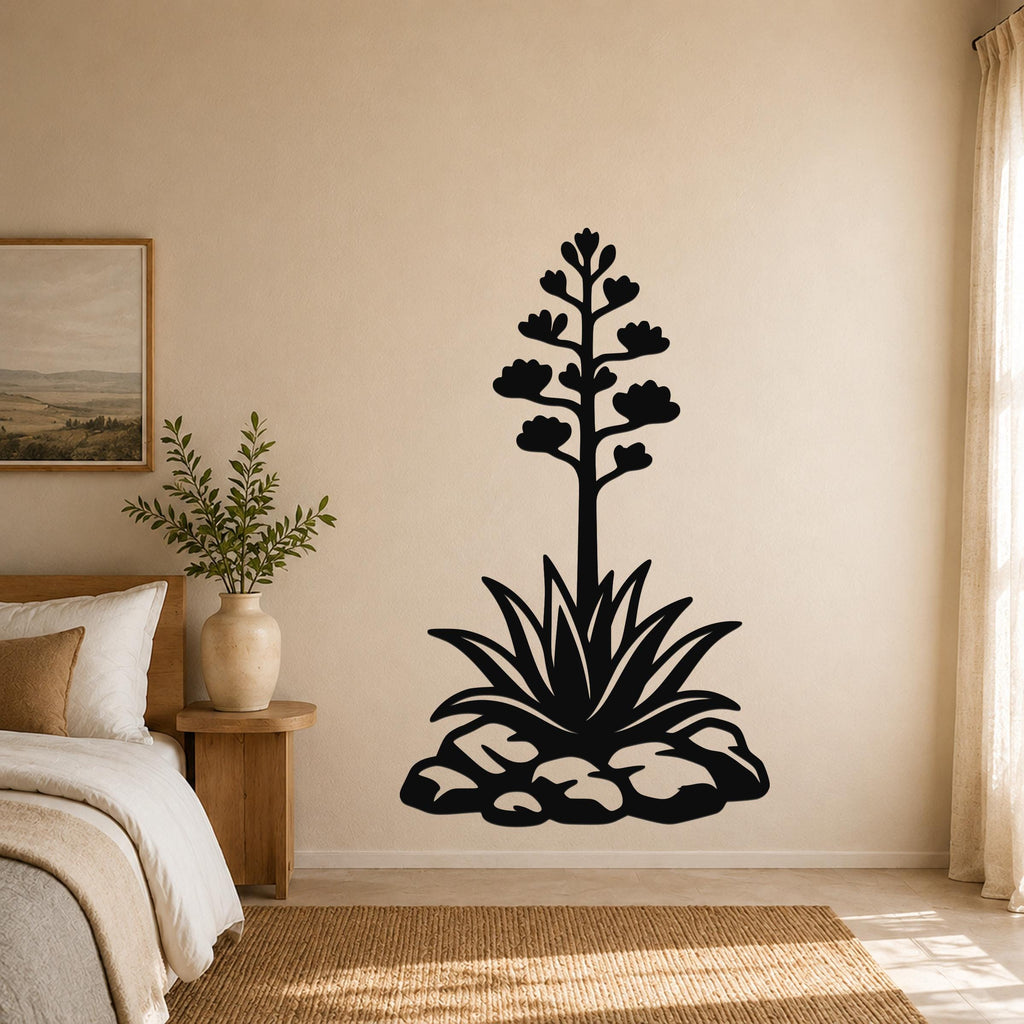 Black metal agave wall sculpture with blooming flower and leaf cutouts, mounted on a beige bedroom wall above a bed.