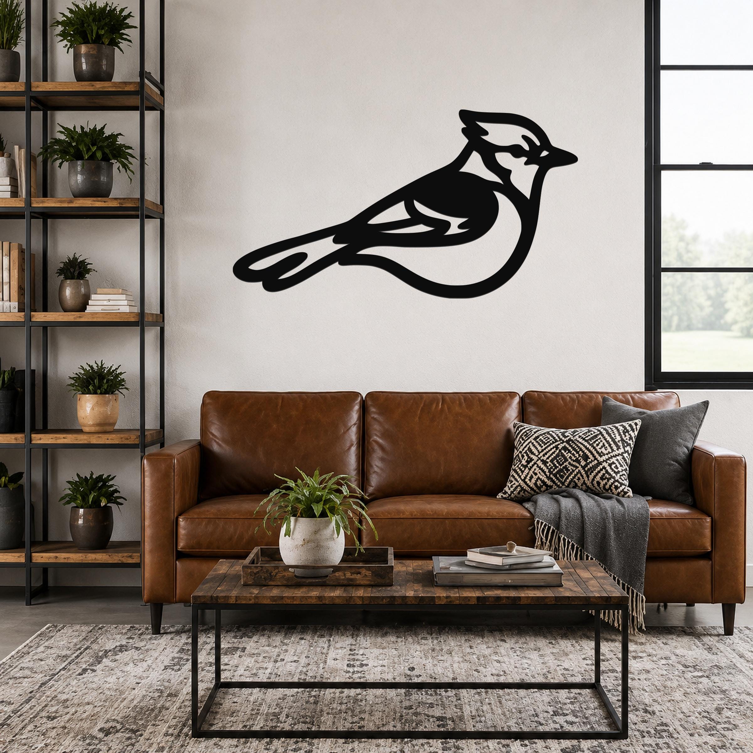 Black metal blue jay wall art silhouette with internal cutout details, mounted above a brown leather sofa in a living room.