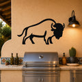 Black metal buffalo wall art silhouette mounted on a stucco wall above a stainless steel grill in an outdoor kitchen.