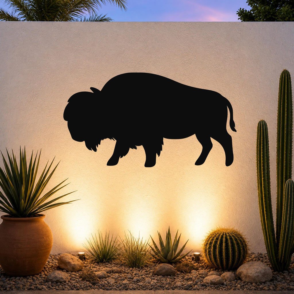 Black metal bison silhouette wall art mounted on a light-colored outdoor wall above a desert garden with cacti and ground lights.