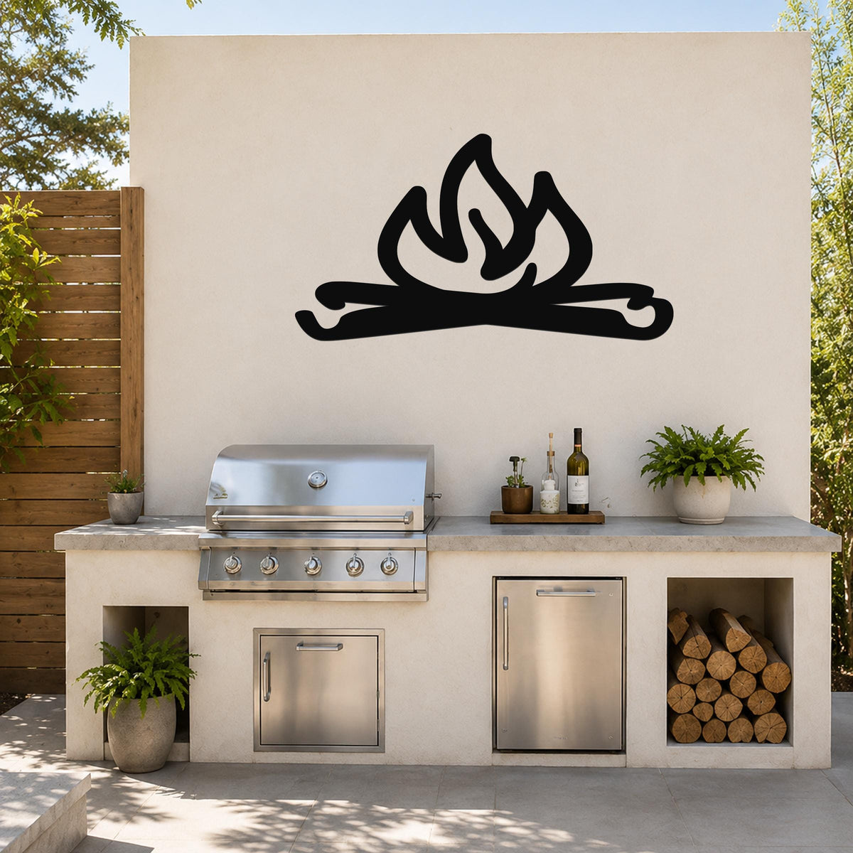 Black metal campfire wall art with flame and log cutouts, mounted on an outdoor kitchen wall above a stainless steel grill and counter.