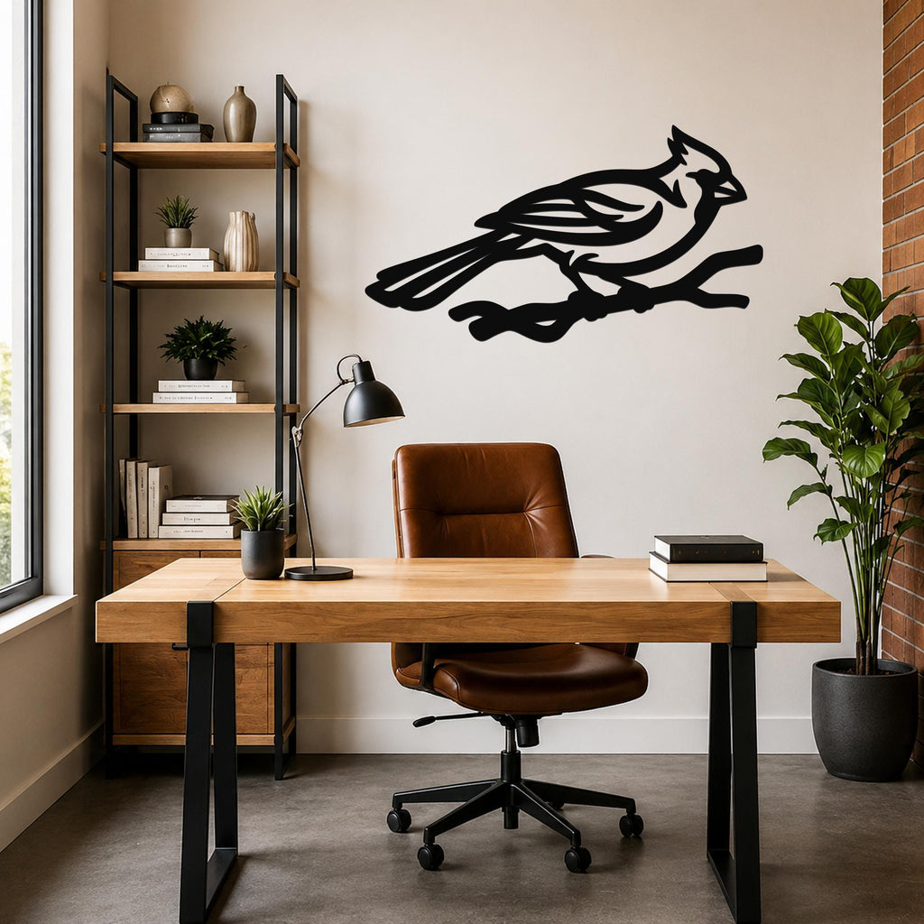 Black metal cardinal wall art in a bold silhouette with internal branch cutouts, mounted on a wall above a wooden desk in a modern home office.