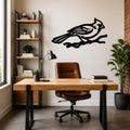 Black metal cardinal wall art in a bold silhouette with internal branch cutouts, mounted on a wall above a wooden desk in a modern home office.