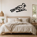 Black metal cardinal wall art in a minimalist silhouette style, mounted above a bed in a bright bedroom.