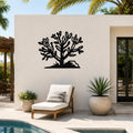 Black metal Cholla cactus wall art with branching cutouts, mounted on a white outdoor wall above a lounge chair near a pool.