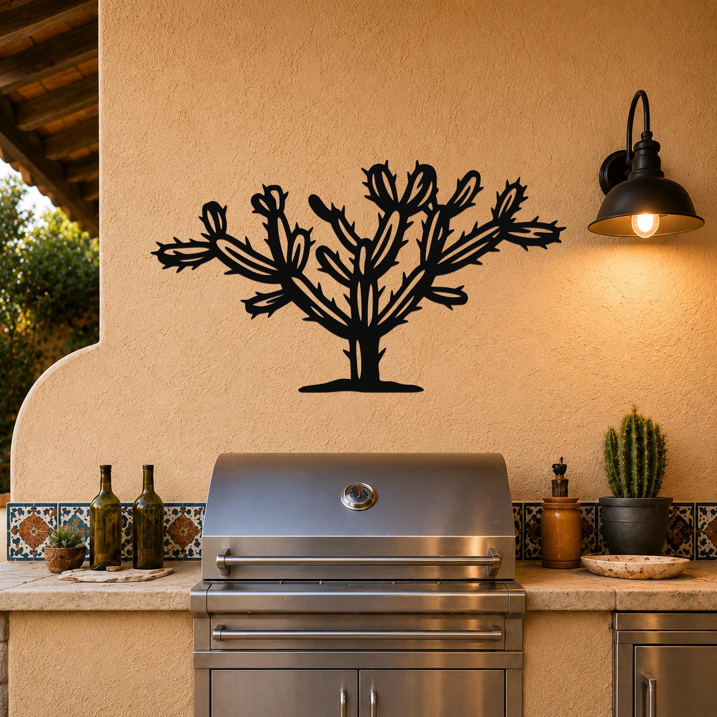 Black metal Cholla cactus wall art with branching silhouette cutouts, mounted on a stucco outdoor wall above a stainless steel grill.
