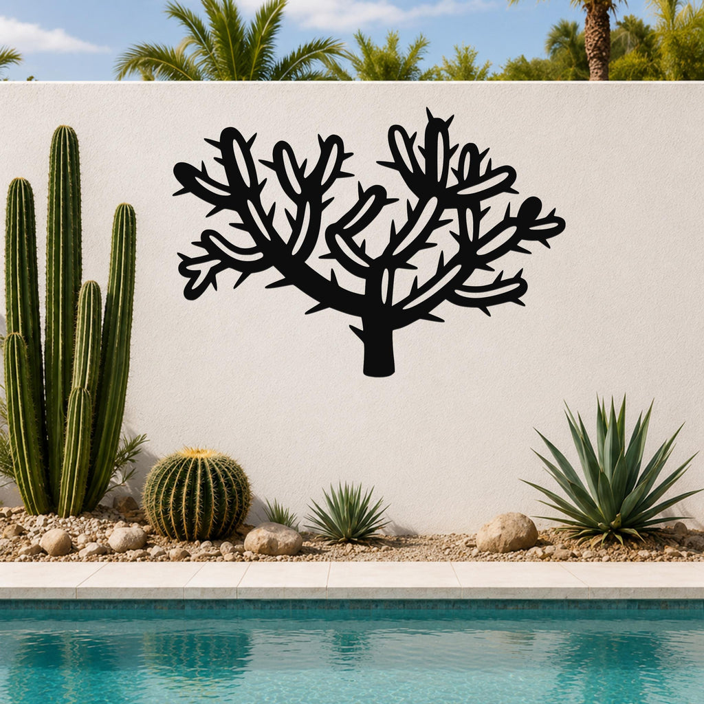 Black metal Cholla cactus wall art with branching spines and cutout details, mounted on a white outdoor wall beside a pool and desert plants.