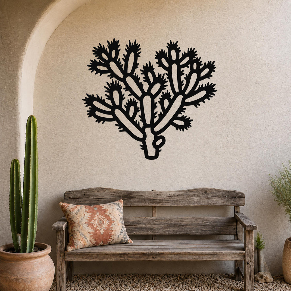 Black metal Cholla cactus wall art with spiny branch cutouts, mounted on a stucco wall above a wooden bench in a southwestern-style patio.