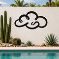 Black metal cloud wall art with flowing silhouette design, mounted on a white outdoor wall beside a pool and desert plants.