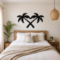 Black metal wall art featuring two crossed palm trees forming a heart shape, mounted above a wooden bed in a coastal-style bedroom.