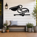 Black metal pelican wall art in silhouette style, mounted on a white shiplap wall above a wooden bench on a porch.