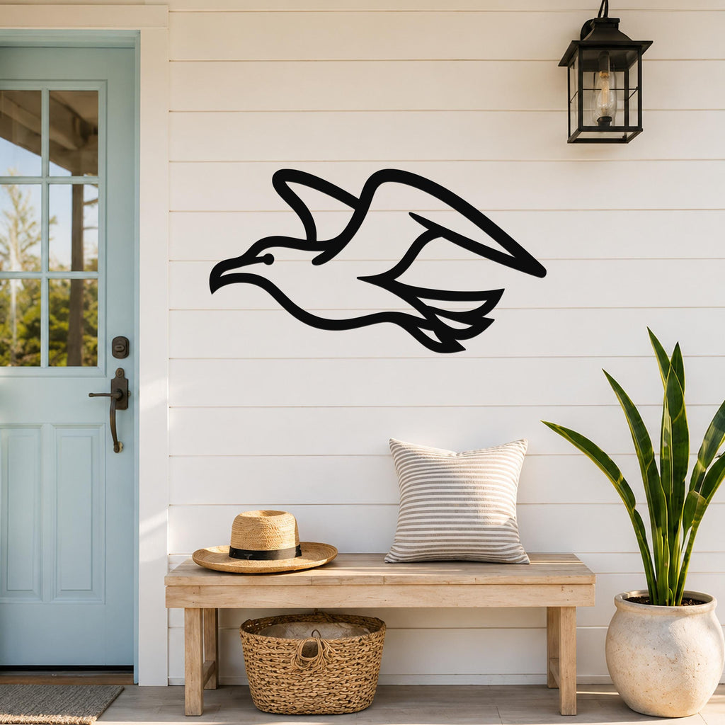 Black metal seagull wall art with a silhouette design, mounted on a white shiplap wall above a wooden bench in a coastal entryway.