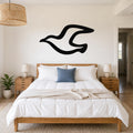 Black metal seagull wall art with a flowing silhouette, mounted above a wooden bed in a bright bedroom.