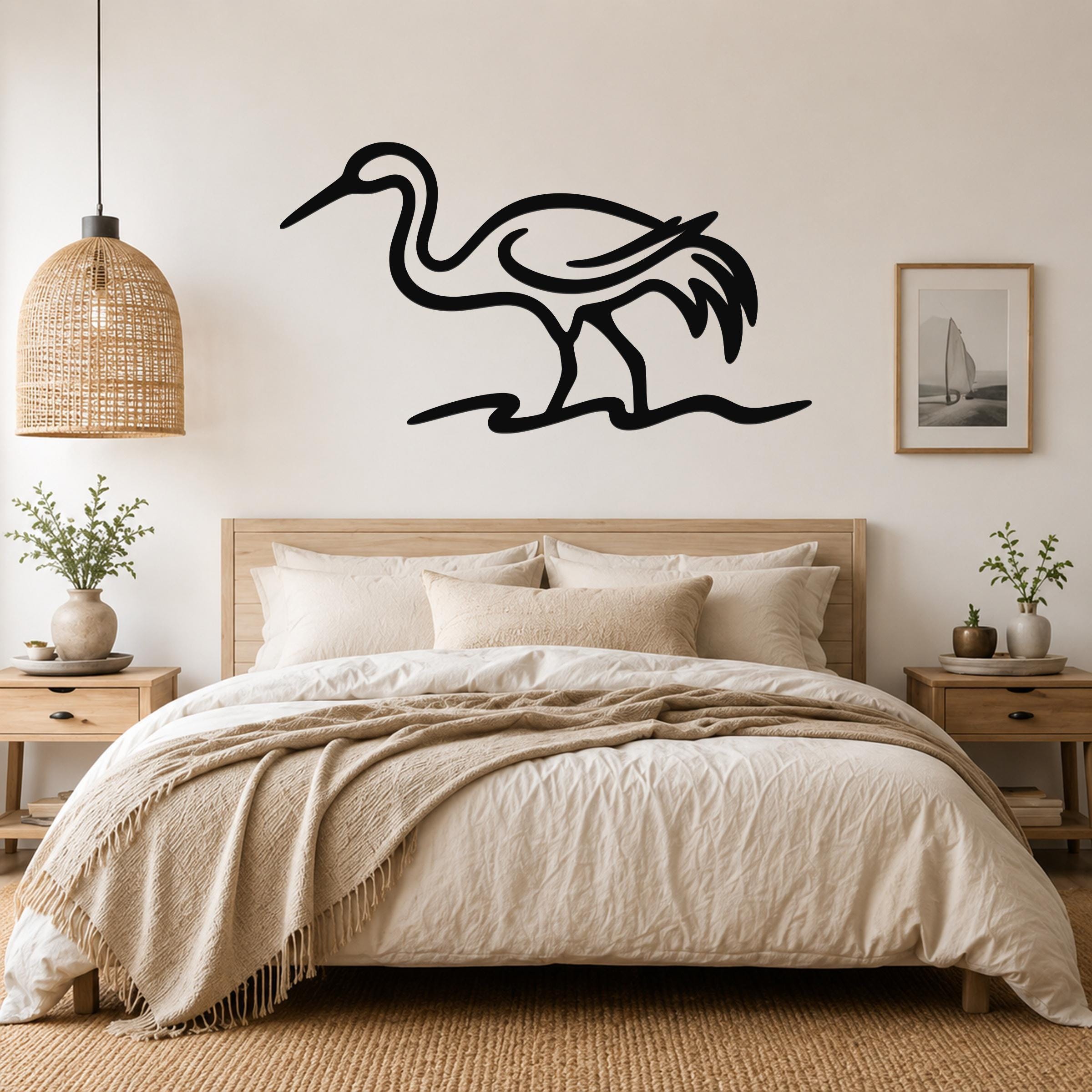 Black metal crane wall art with flowing line cutouts, mounted above a bed in a neutral bedroom.