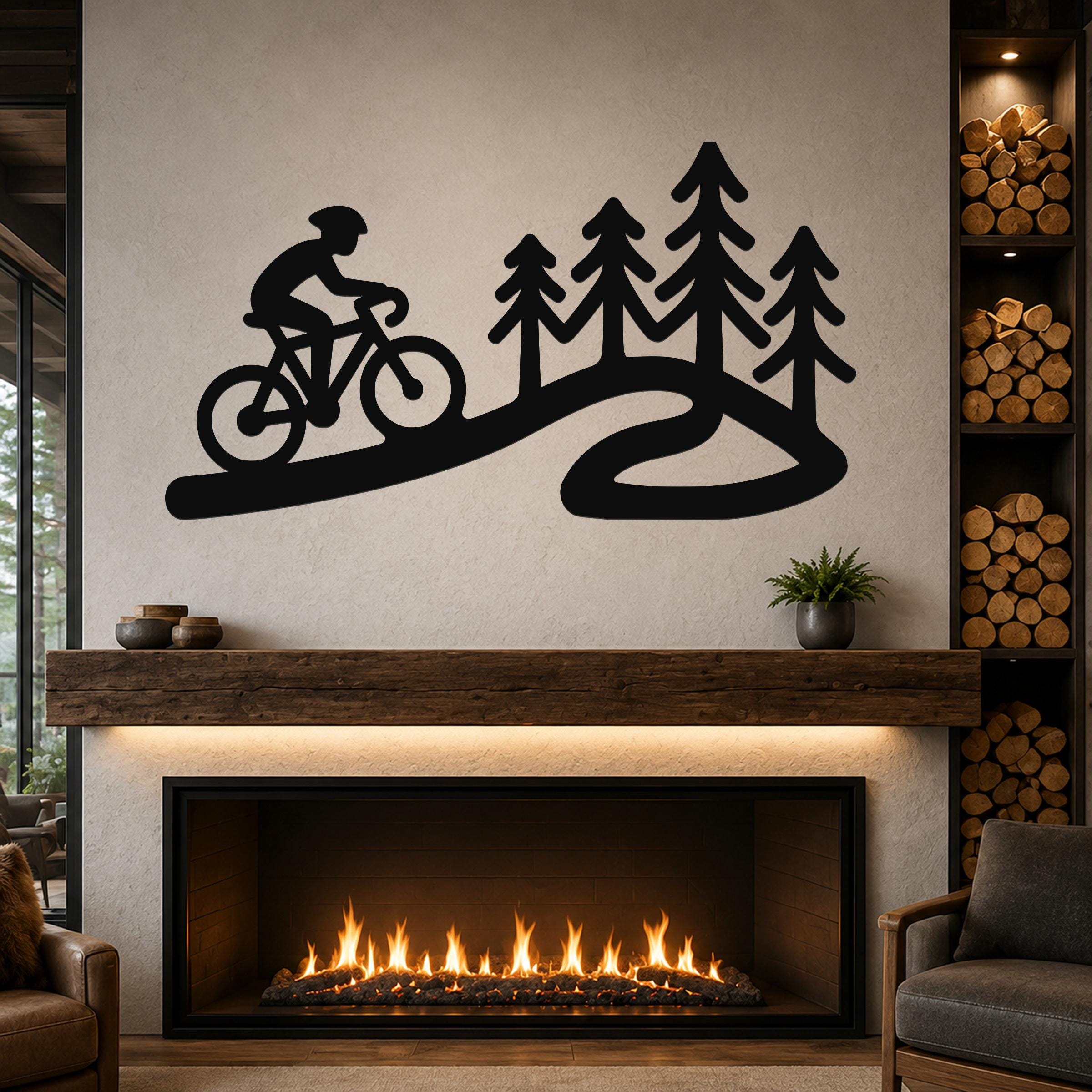 Black metal wall art silhouette of a cyclist on a winding path with pine trees, mounted above a fireplace in a living room.