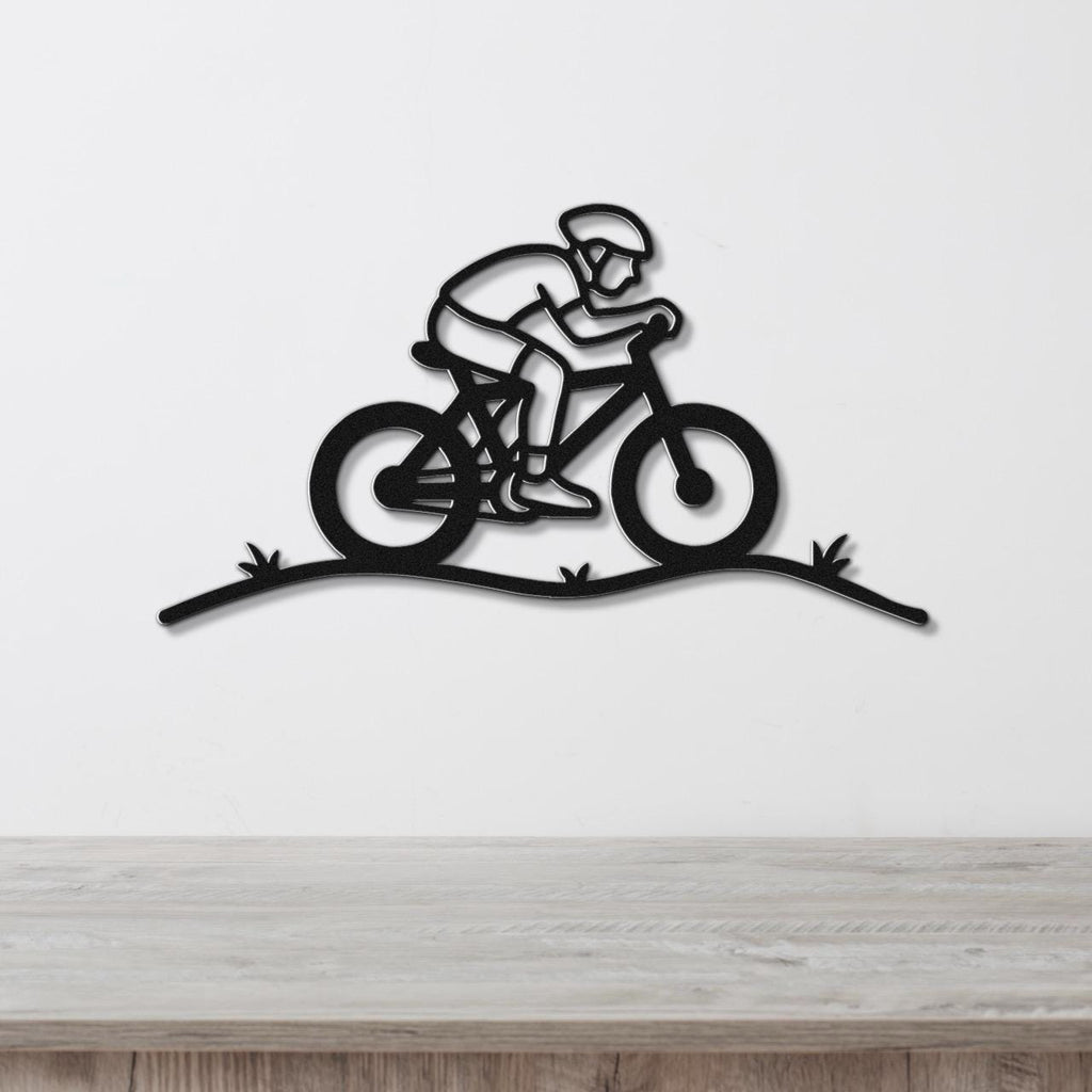 Black metal wall art featuring a minimalist cyclist silhouette in motion, mounted on a white wall above a wooden surface.