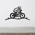 Black metal wall art featuring a minimalist cyclist silhouette in motion, mounted on a white wall above a wooden surface.
