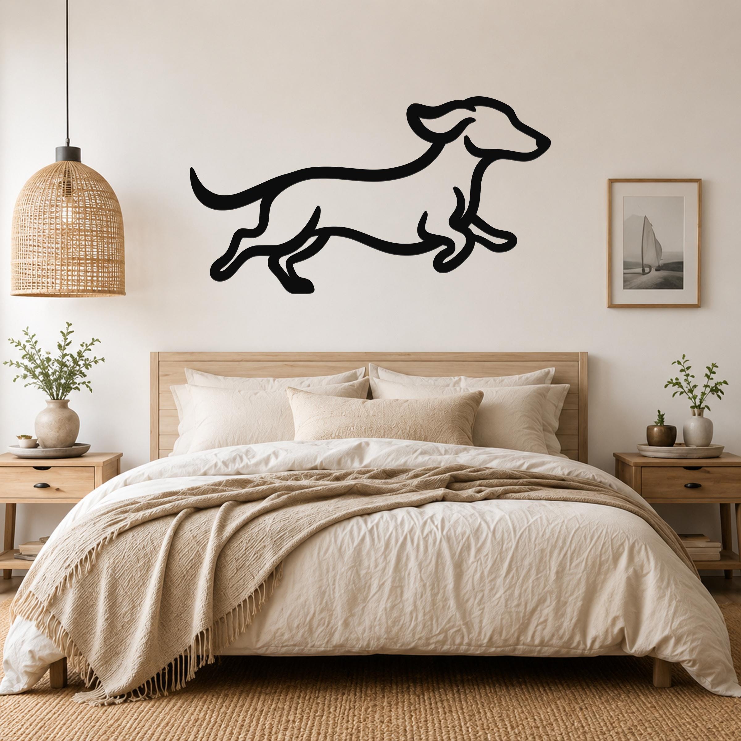 Black metal dachshund wall art in a running silhouette, mounted above a bed in a neutral bedroom.