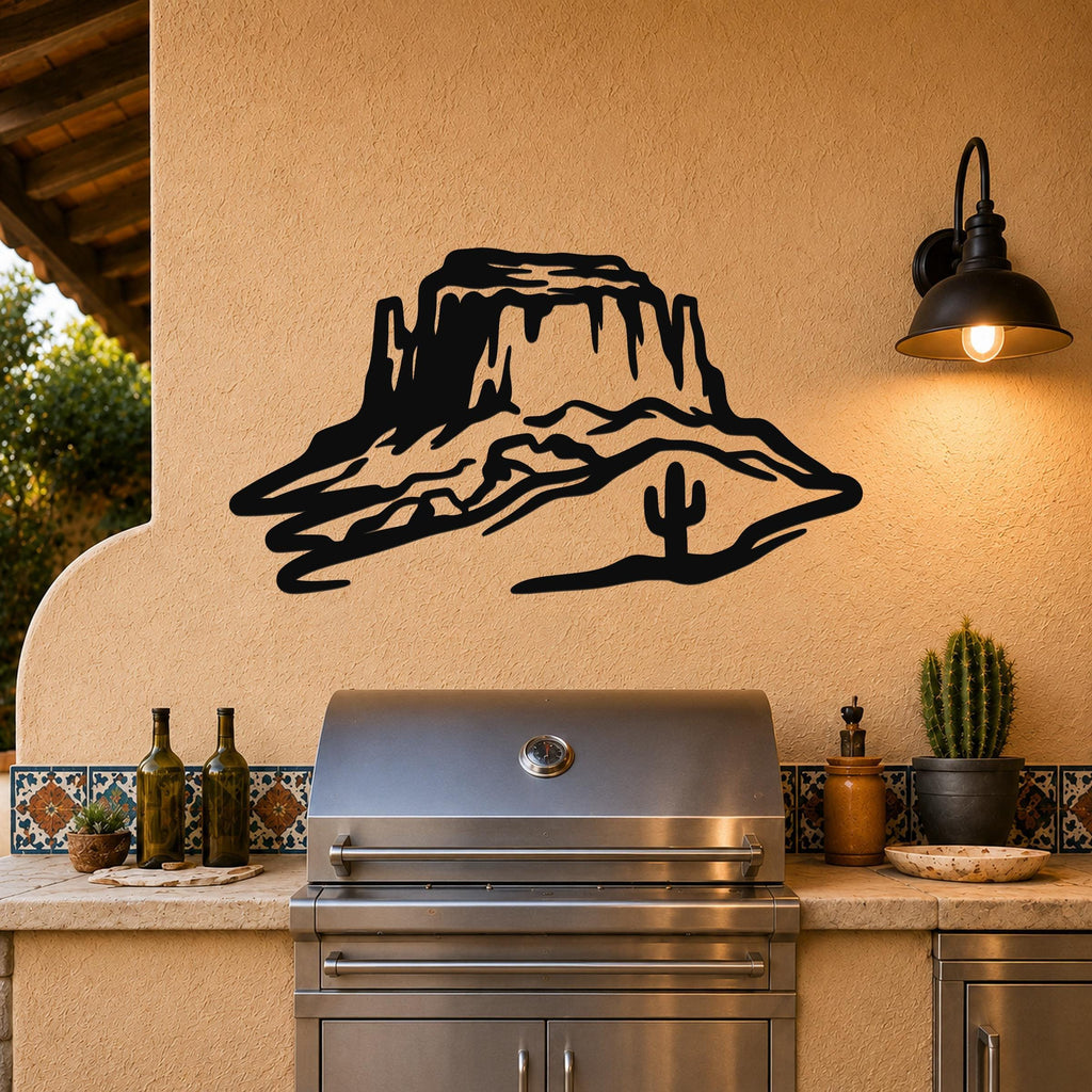 Black metal wall art silhouette of a desert mesa with a cactus, mounted on a stucco wall above a stainless steel grill on an outdoor patio.