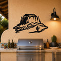 Black metal wall art silhouette of a desert mesa with a cactus, mounted on a stucco wall above a stainless steel grill on an outdoor patio.