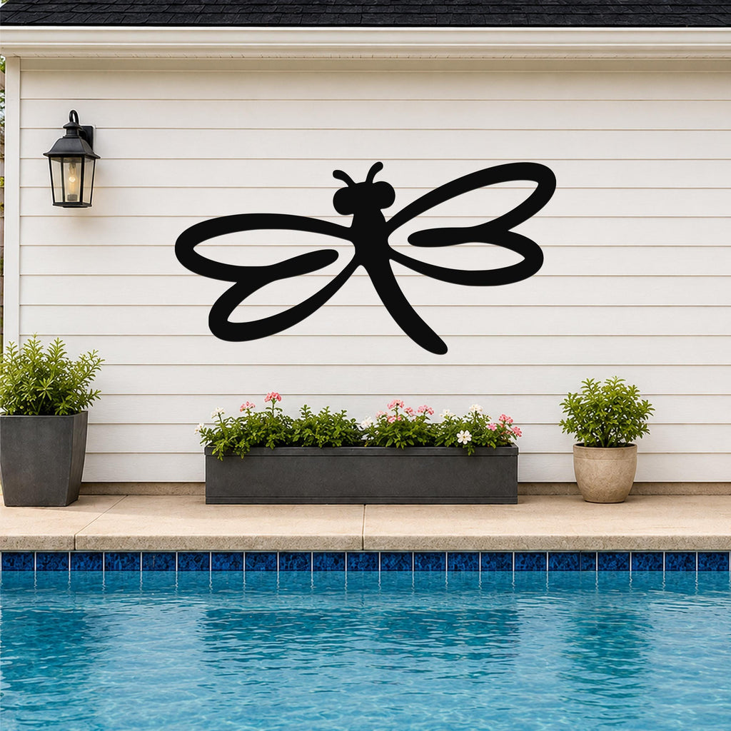 Black metal dragonfly wall art with flowing wing cutouts, mounted on a white horizontal siding wall above a poolside planter.