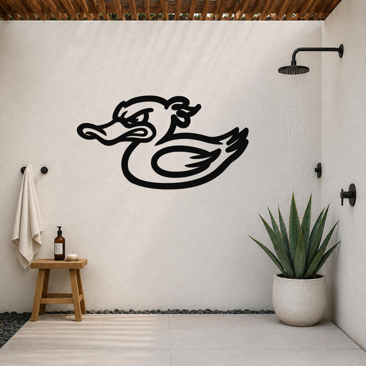 Black metal duck wall art with a bold silhouette design, mounted on a white outdoor shower wall above a small wooden stool and a potted succulent.