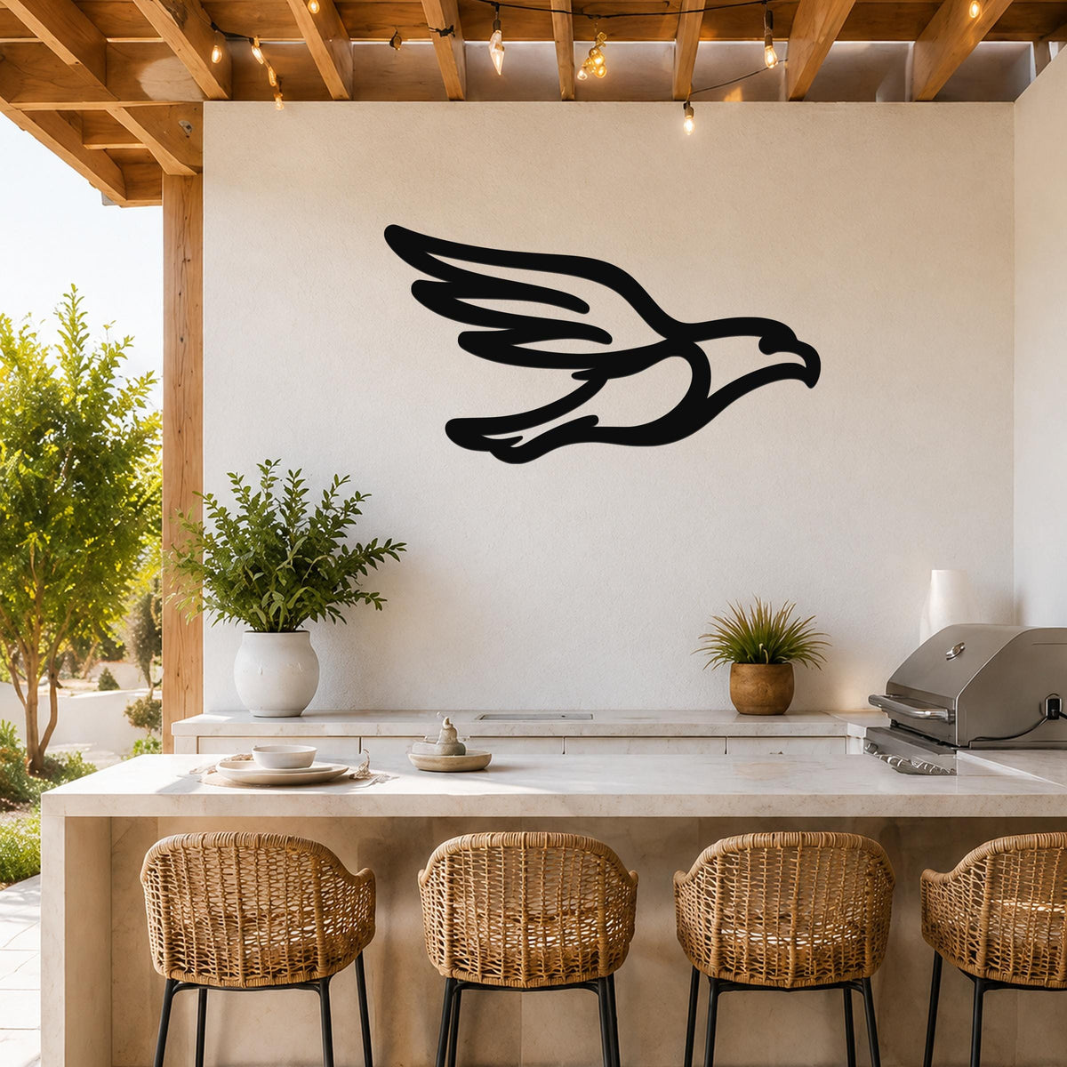Black metal eagle wall art with a bold silhouette design, mounted on a white outdoor wall above a kitchen counter with wicker bar stools.